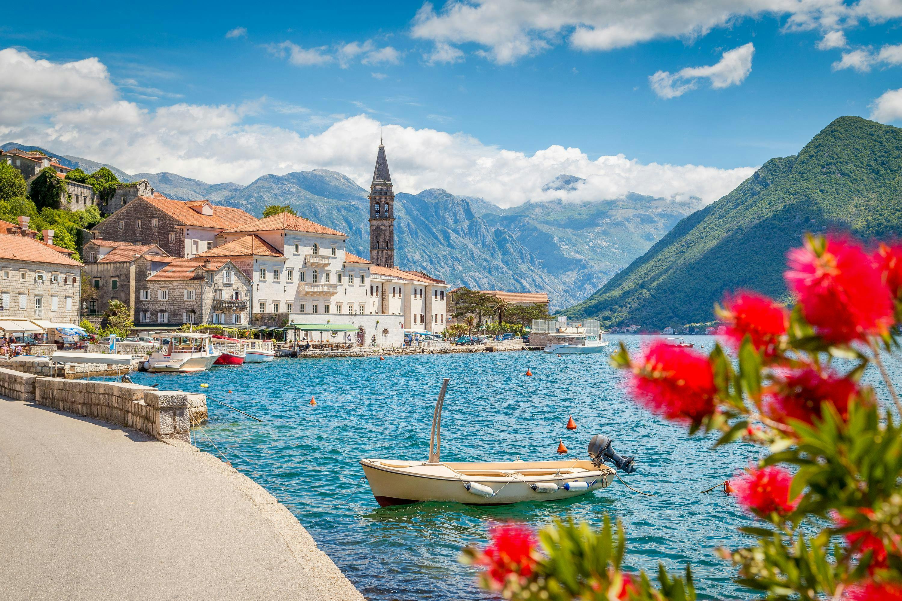 Scenic panorama view of the historic town of Perast at famous Bay of Kotor with blooming flowers on a beautiful sunny day with blue sky and clouds in summer, Montenegro, southern Europe