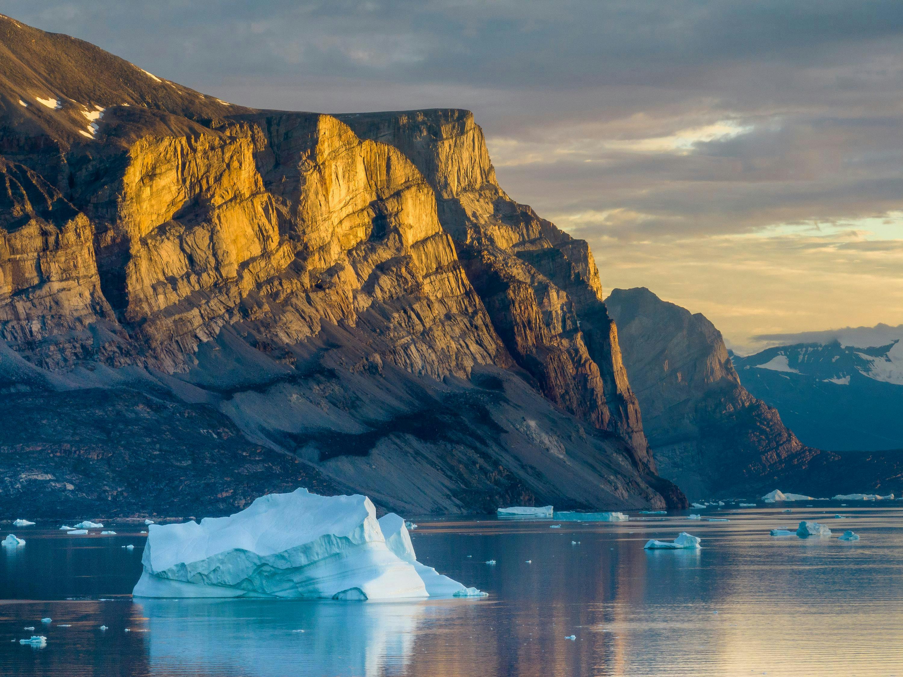 Greenland, Avannaata Municipality,  Setting midnight sun lights cliffs of Storøen Island along Alanguarqap Suvdlua strait near Uummannaq on summer evening