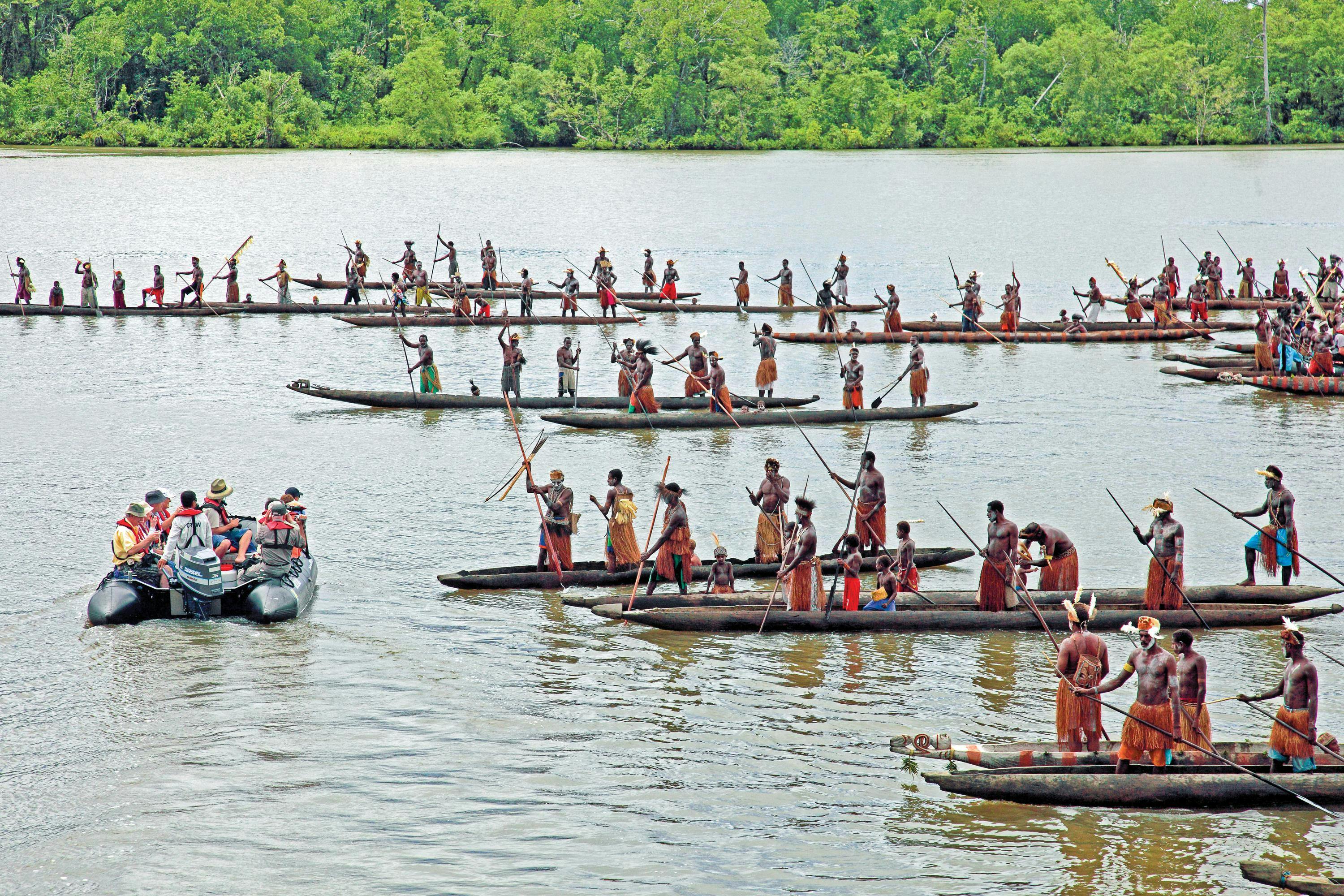 Asmat Melanesian men in traditional decoration, paddling dug-out canoes, to greet guests arriving by zodiac in Syuru, Papua, Indonesia New Guinea.